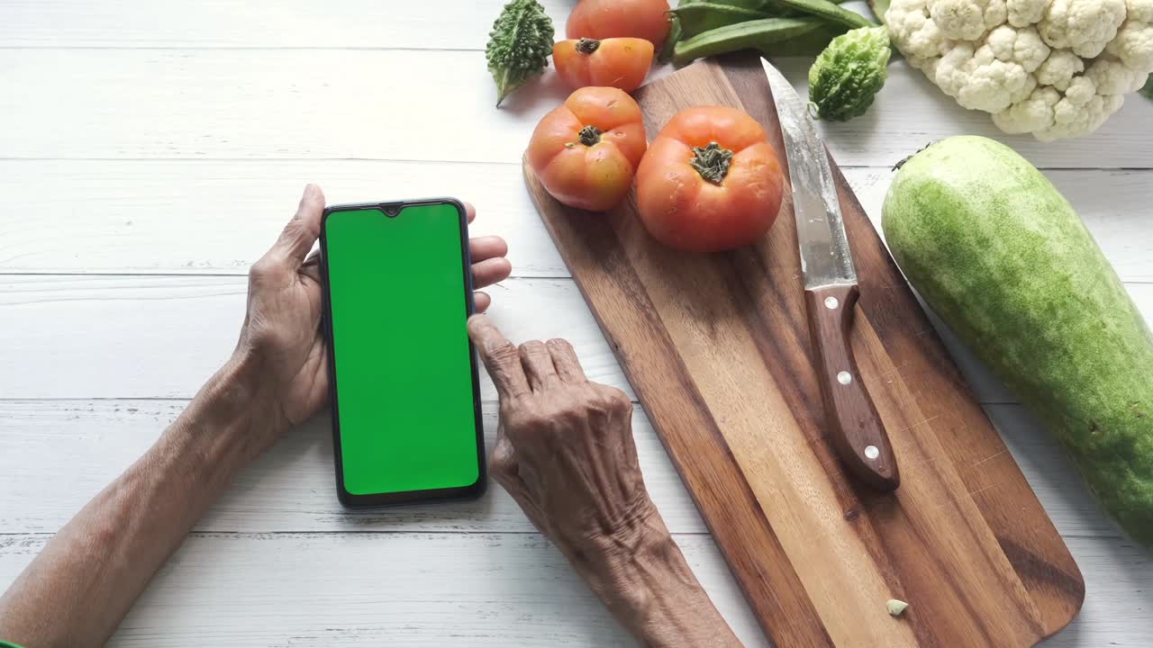 mujeres mayores mano usando teléfono inteligente y verduras frescas en la mesa