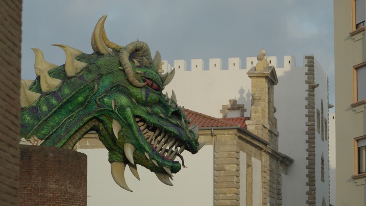 Maestosa scultura di drago verde con corna dorate e denti affilati si erge come guardiano mitico vicino a una storica torre del castello. Statua tradizionale protettrice della città spagnola a Gijón, nelle Asturie