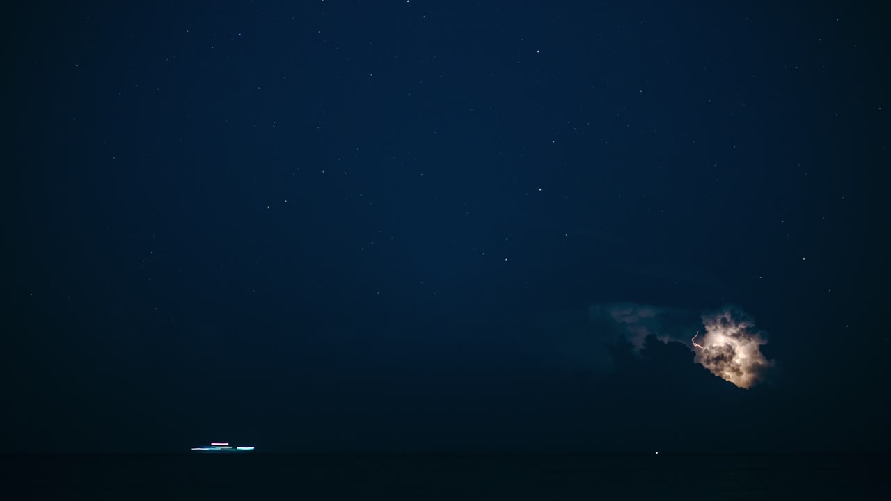Timelapse of large thunderstorm clouds at night in the sea. Lightning strikes and ships passing. Long exposure timelapse.