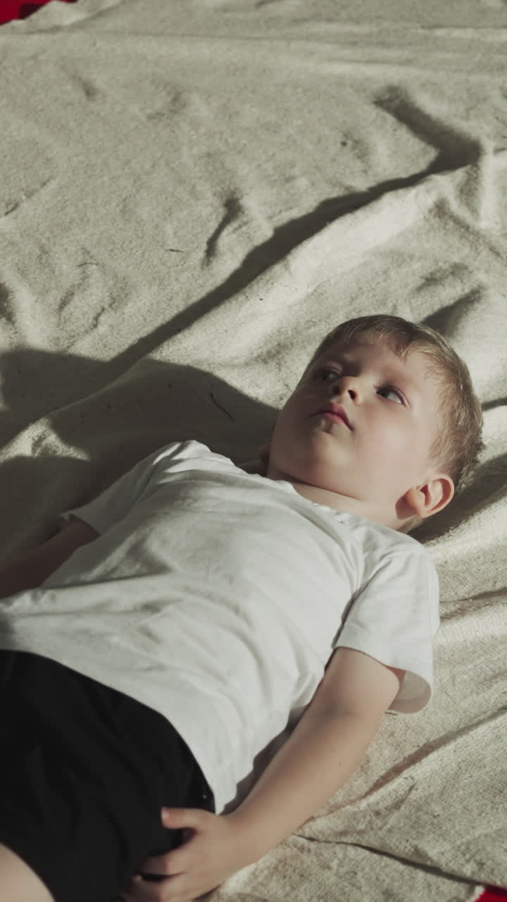 아이는 휴식 시간 동안 권투 체육관에서 카에 앉아 있습니다. 심각한 유아 소년은 전투 스포츠 클럽에서 싱 가방 근처에 누워 있습니다. 아이는 몸을 편안하게합니다.