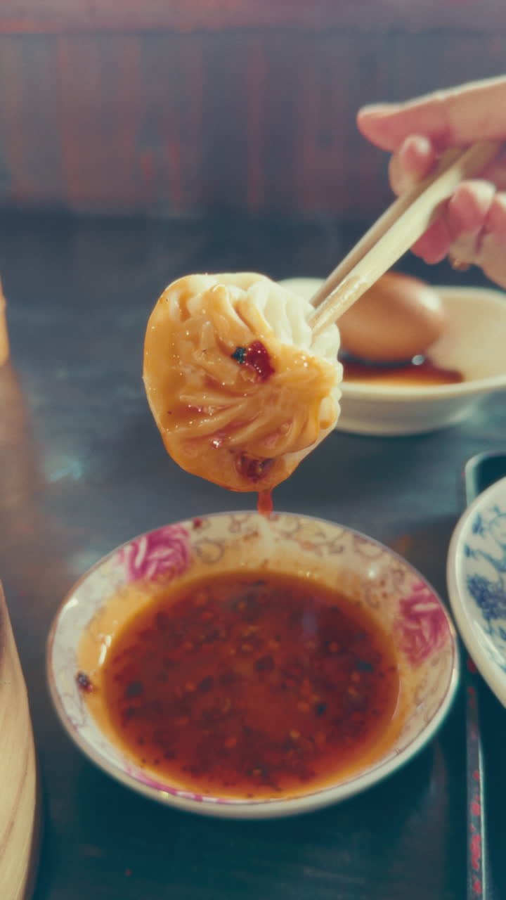 Hand holding a dumpling with chopsticks and dipping sauce