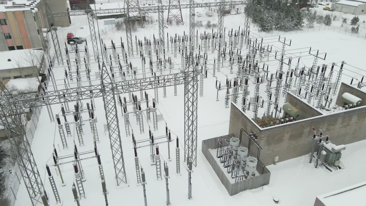 Wide aerial orbit over a large electrical substation in extreme winter conditions, showing snow covered insulators, transformers, and power lines under clear cold daylight
