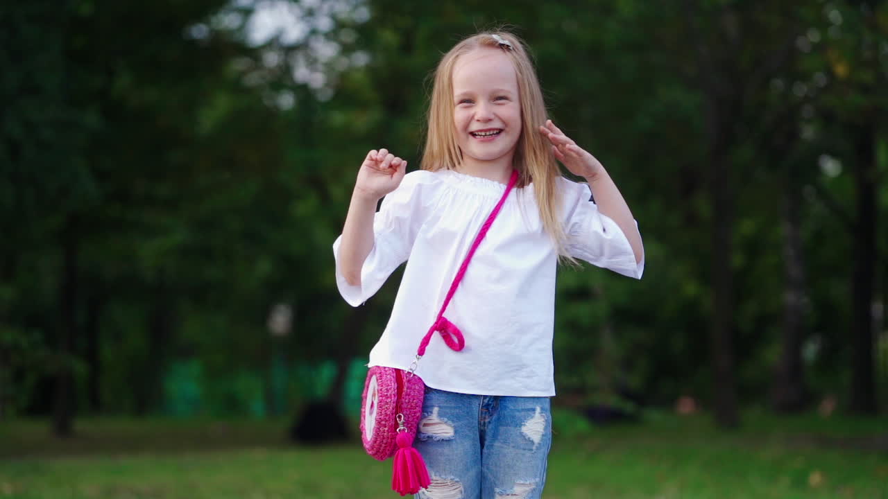 Portrait of a happy kid in the green park. Pretty little girl smiling and looking at camera on green natural background outdoors. Slow motion.