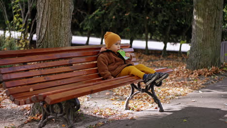 approaching the little kid sitting on the bench in the park. cute baby having a snack on the walk.