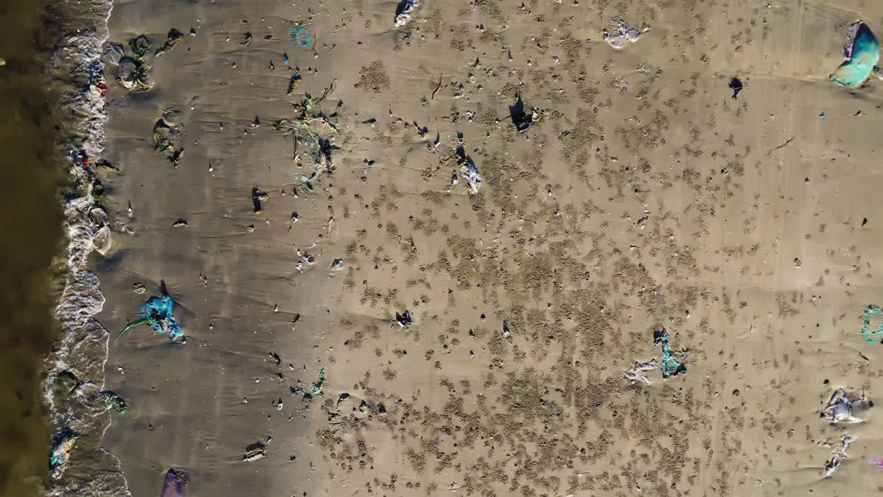 Aerial top down, polluted beach with plastic trash on shore