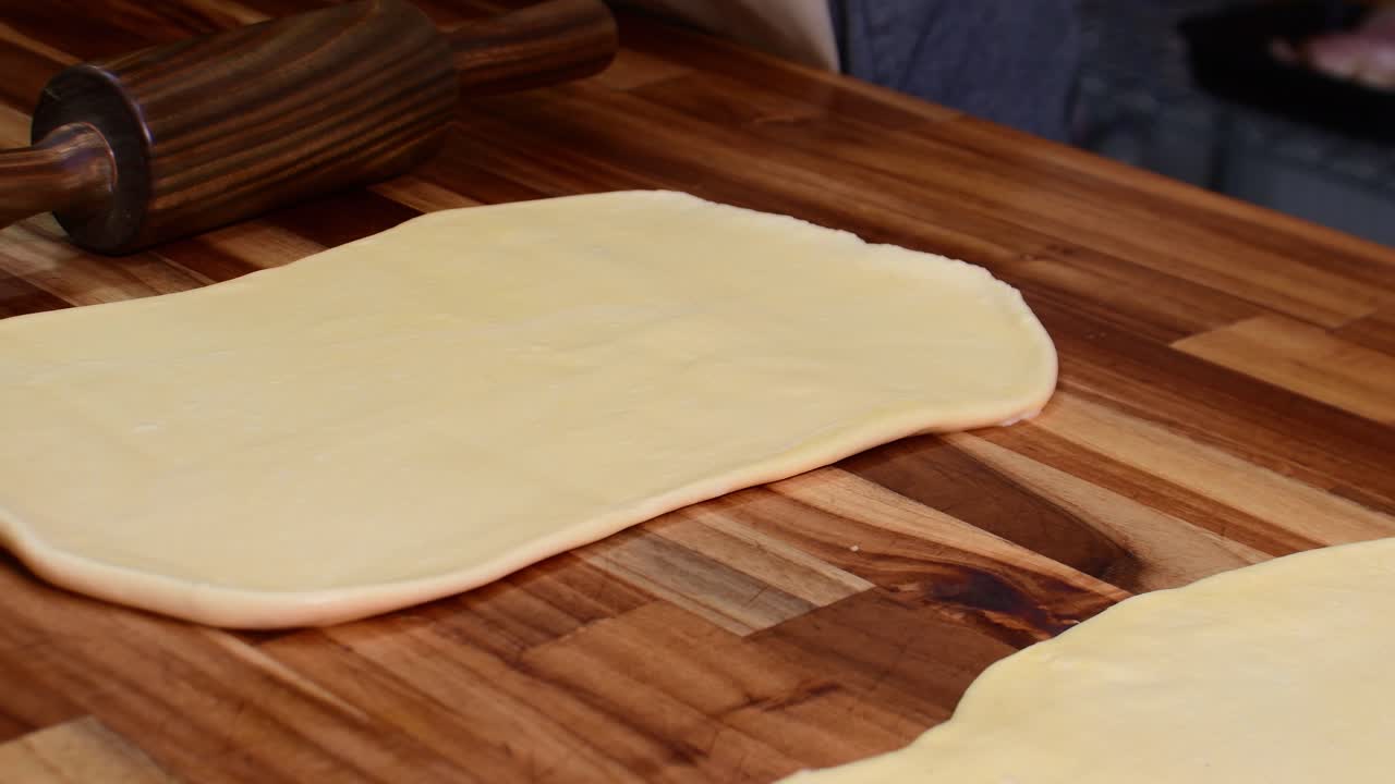 Man flattens fresh dough with a wooden rolling pin on a bakery table