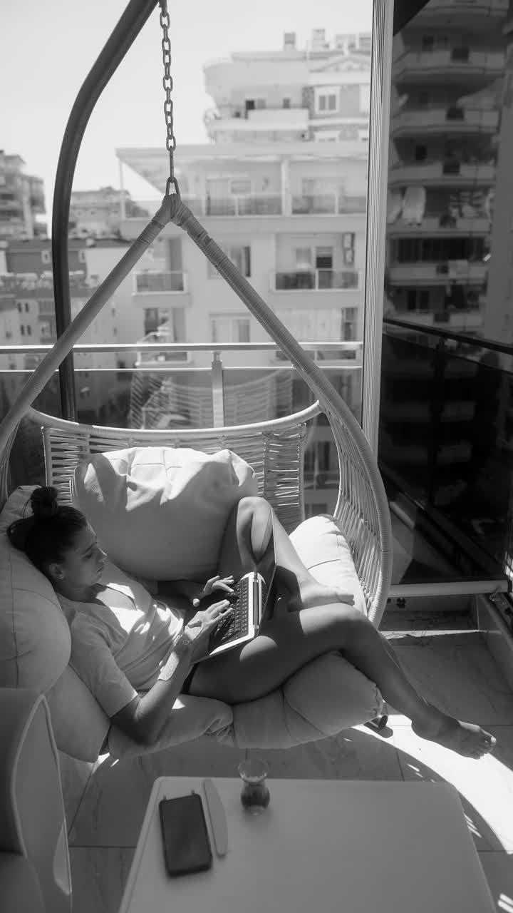 mujer trabajando en una computadora portátil en un columpio de balcón