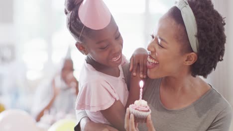 african american mother and daughter celebrating birthday blowing out candle on cake, slow motion