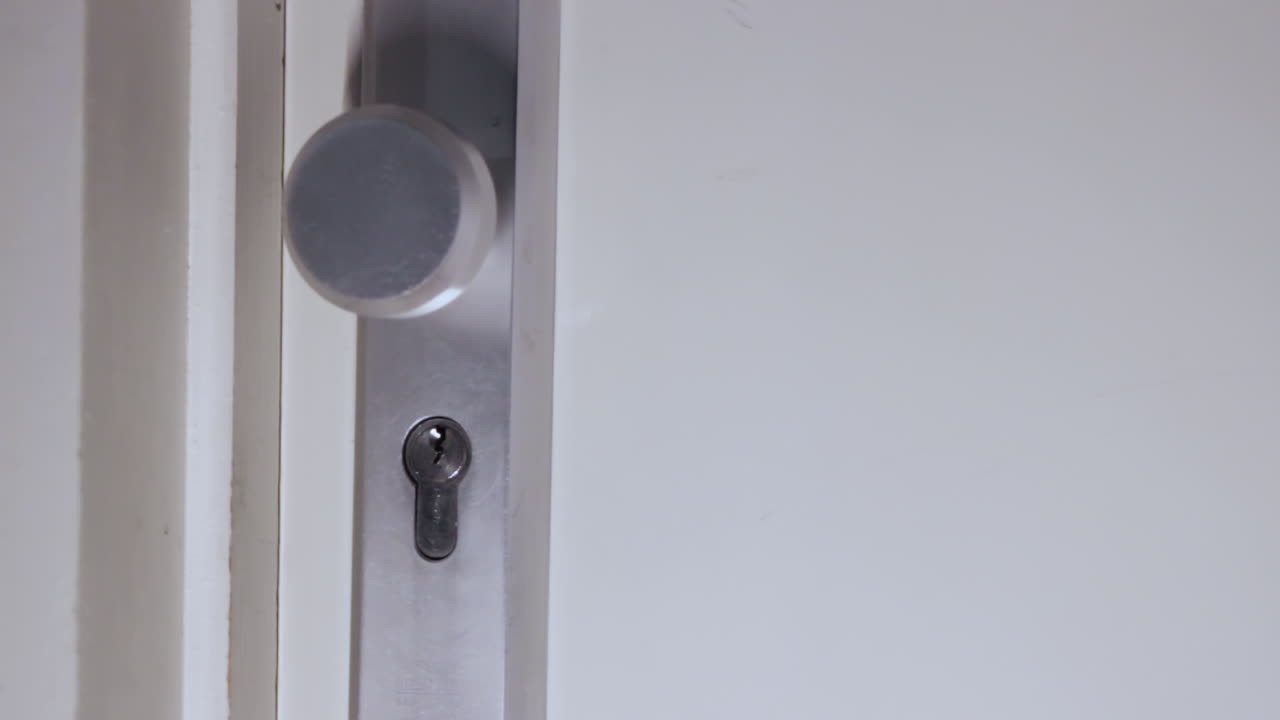 Close up shot of a shadowy figure opening a door with a set of keys and wearing gloves