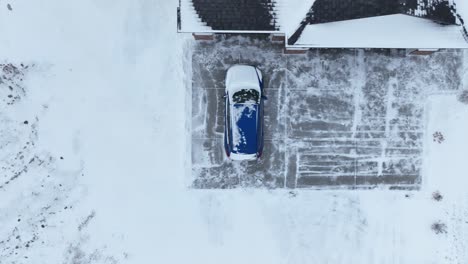 overhead drone shot of a car covered in snow in a frozen driveway