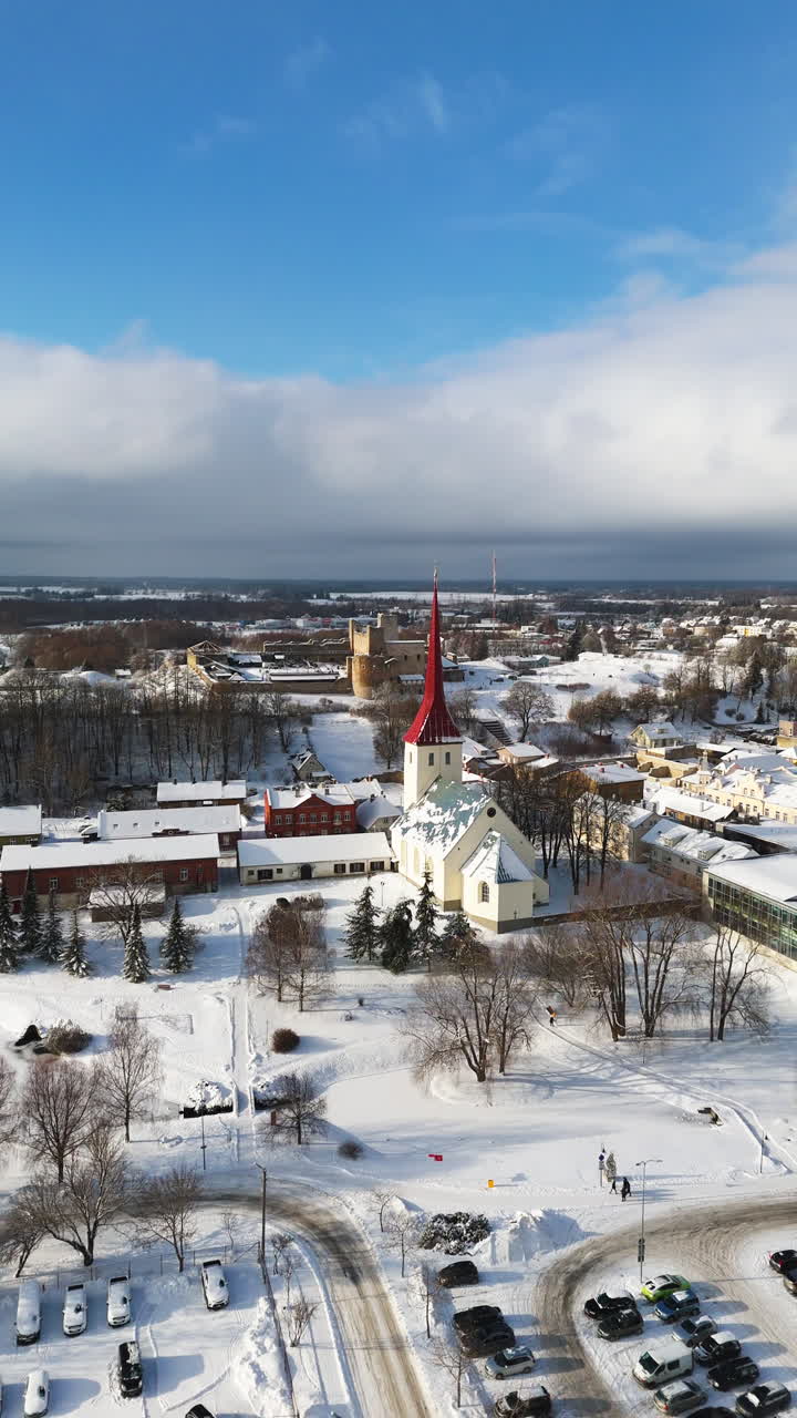 Vertikal drönarbild runt den snöiga kyrkan, slott i bakgrunden, vinter i Rakvere