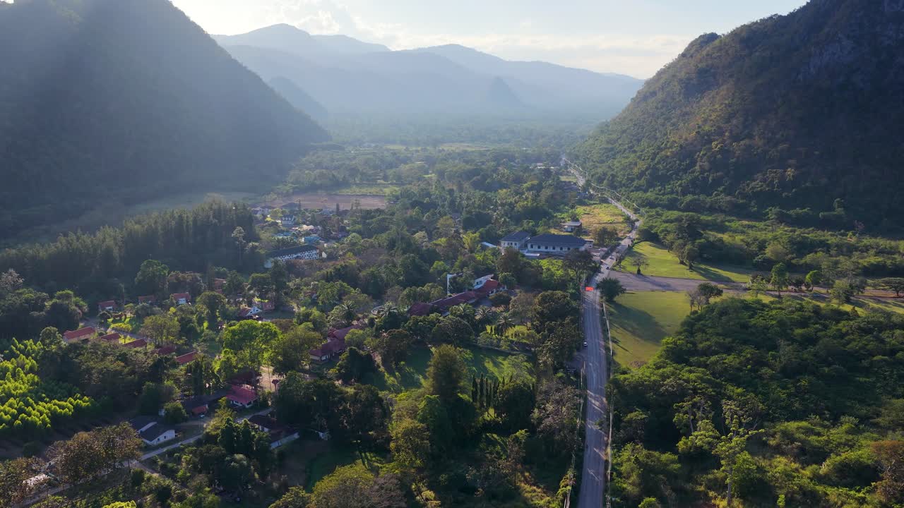 Drone sobrevoa um vale exuberante com montanhas sob os raios dourados do pôr do sol na Tailândia