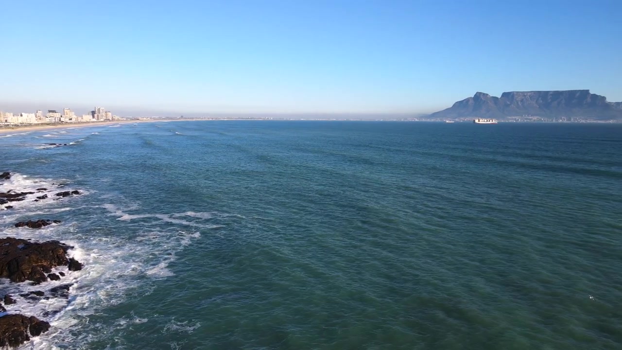 Küstengemeinde und Küstenlinie von Bloubergstrand in Richtung Tafelberg, Drohnen-Schwenk.