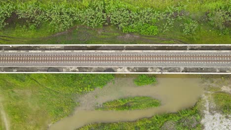 descending aerial footage revealing the elevated railway, marshland with green grass and brown water from heavy rain in muak klek, saraburi, thailand