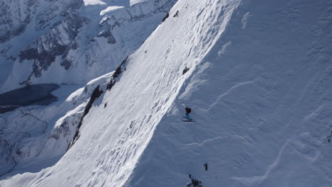 Drone-shot-showing-extreme-skier-sliding-down-snowy-slope-of-mountain-in-sunlight