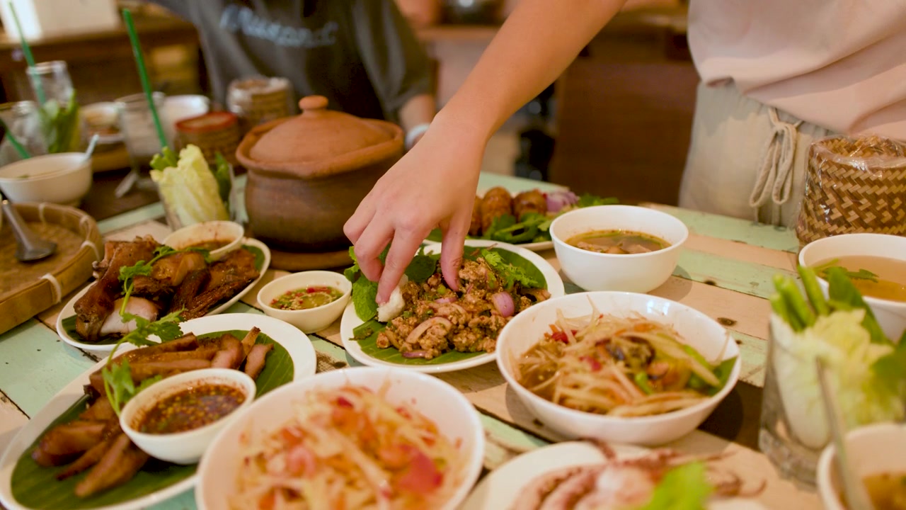 Close-up tangan mencelupkan nasi ketan ke dalam salad daging babi cincang saat makan