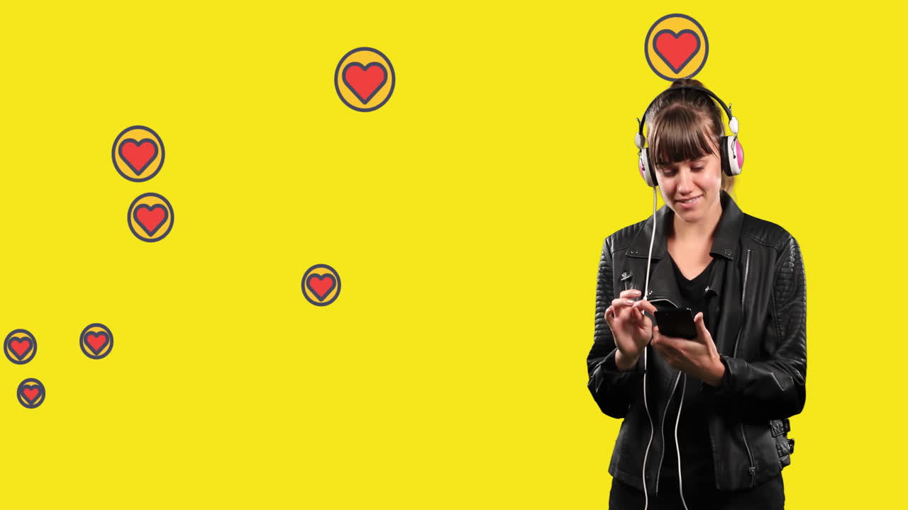 mujer usando un teléfono inteligente y escuchando música contra iconos de corazón flotando en un fondo amarillo