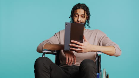 hombre en silla de ruedas hablando con un amigo a través de internet videocall usando tableta