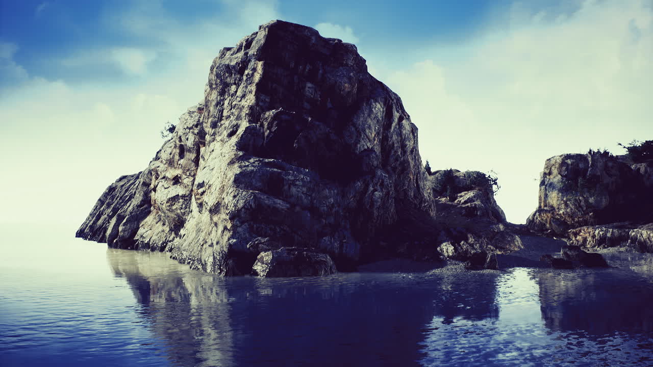 Majestic rocky outcrop mirrored in tranquil coastal waters at sunrise