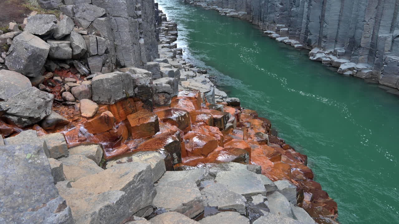 가파른 암석 기둥 사이를 흐르는 녹색의 거대한 강이 있는 주황색 회색 현무암 협곡의 모습
