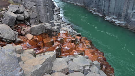 reveal of orange-grey basalt canyon with a green massive river flowing between steep rocky columns