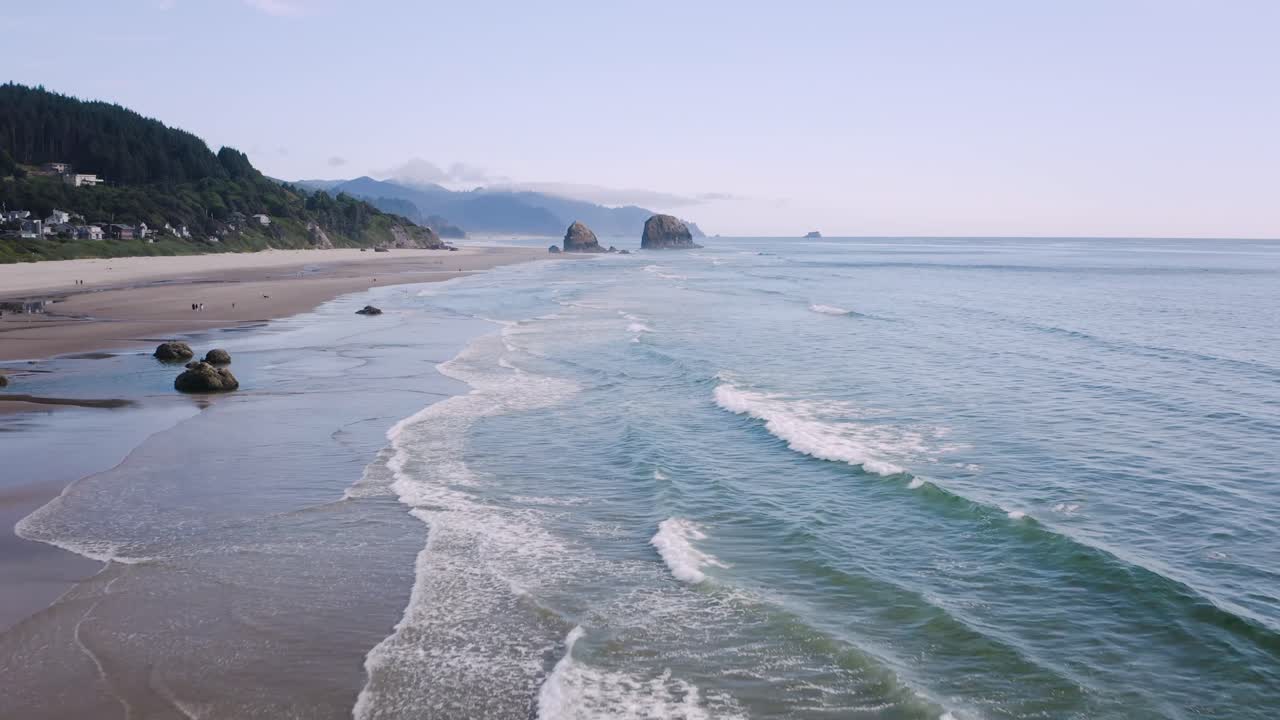 Low tide waves hit the gold sand Cannon Beach on the Oregon Coast. Seastack rock formation on the horizon. Slightly above dolly in drone flight