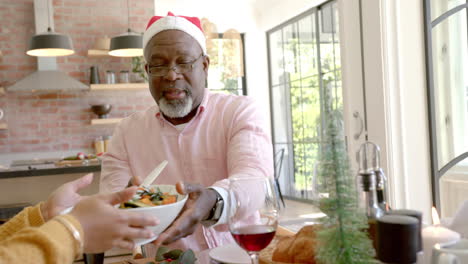 feliz madre afroamericana pasando el plato en la mesa de la cena de navidad de la familia de varias generaciones