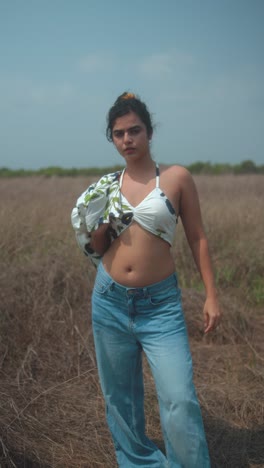 young woman posing in a field, showcasing a stylish outfit with casual jeans