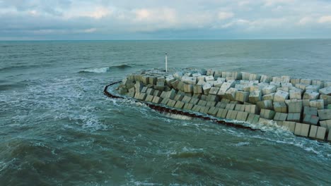 Aerial-establishing-view-of-protective-stone-pier-with-concrete-blocks-and-rocks-at-Baltic-sea-coastline-at-Liepaja,-Latvia,-strengthening-beach-against-coastal-erosion,-drone-shot-moving-back