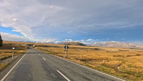 forward-facing dashcam view of a car driving on an empty highway through golden autumn fields, with distant mountains and dramatic sky, in soft daylight