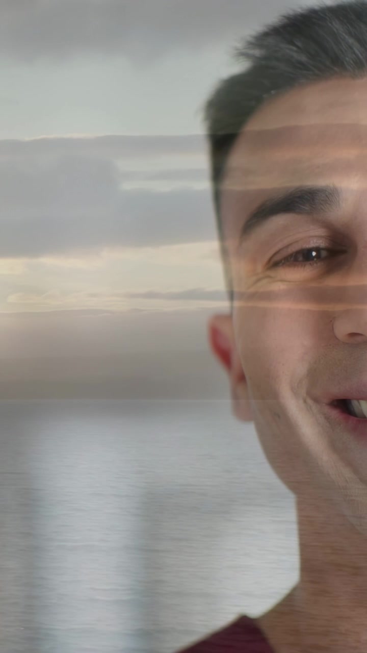 Vertical video: Mid adult man reacting to cue, widening smile as sea overlaying face, marketing