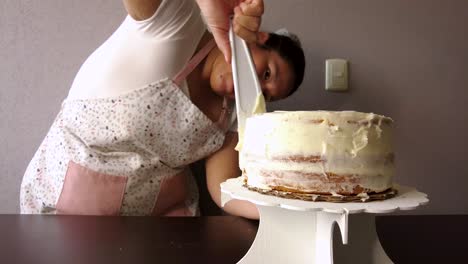 Mujer-Latina-Con-Un-Delantal-Preparando-La-Cocina-Horneando-Un-Pastel-Esparciendo-El-Glaseado-De-Mantequilla-Con-Una-Espátula-Blanca