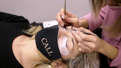 Crop-beautician-with-tweezers-applying-artificial-lash-on-client