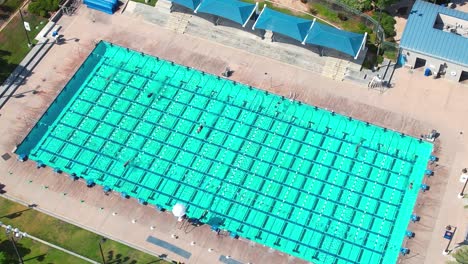 people swimming laps in a large outdoor pool - aerial ascending view