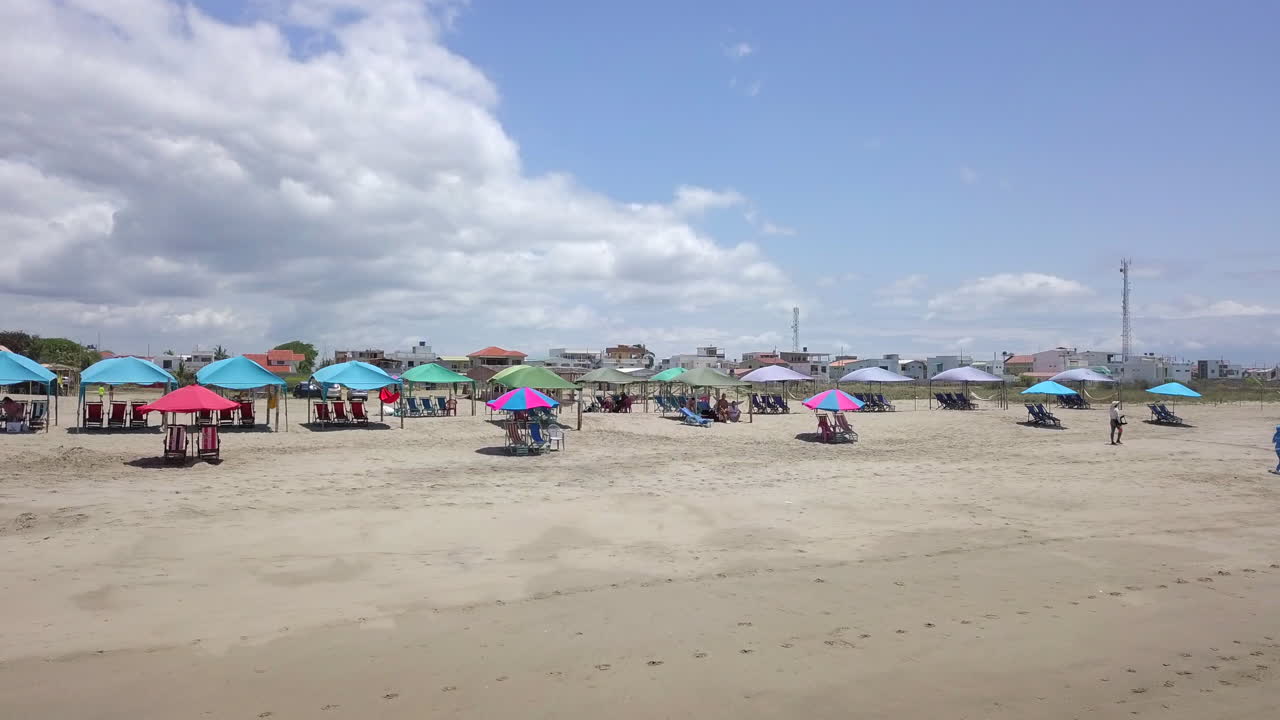 bajo cerca del suelo vuelo de drones disparado hacia carpas y sombrillas con gente en la playa de la ciudad de playas general villamil en ecuador