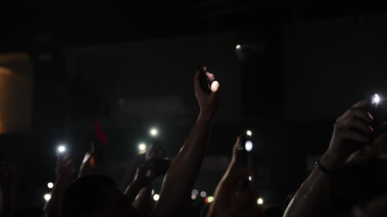 Pubblico con le mani alzate che tiene smartphone, illuminato da luci intense a un concerto