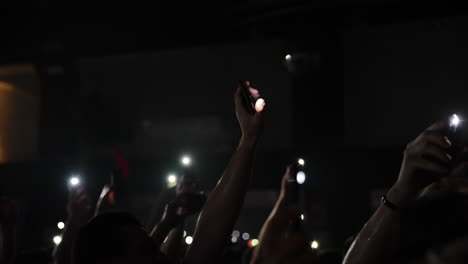 audience with raised hands holding smartphones, illuminated by bright lights at a concert event