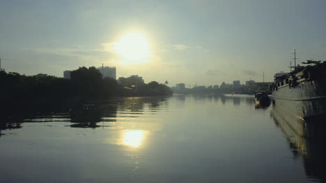 sunrise, reflections and riverboats on the canal near the entrance to the saigon river and port in ho chi minh city vietnam