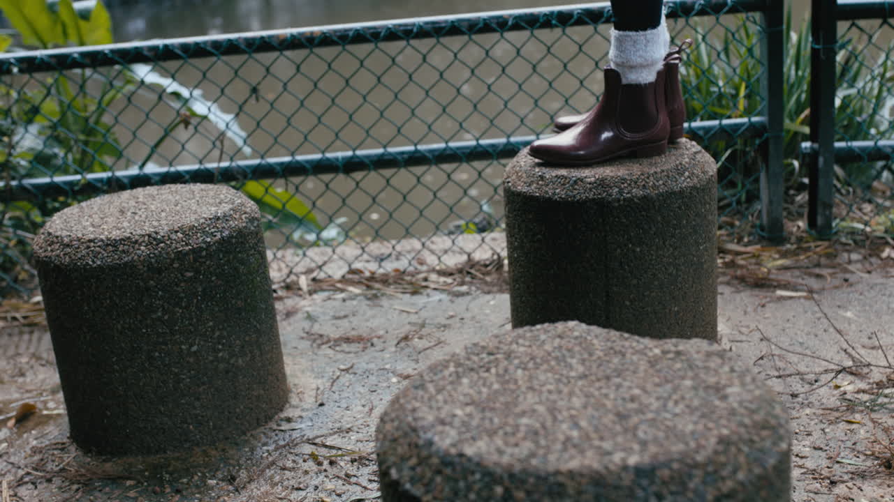 추운 겨울날 비 속에서 노는 것을 즐기며 공원 벤치에서 뛰어다니는 부츠 여자를 닫으세요