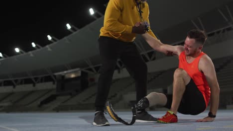 diverse male coach helping tired disabled male athlete with running blade to stand up