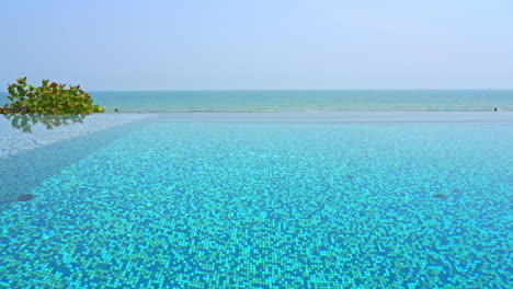 view across surface of clear blue water in infinity edge swimming pool of luxury beachside resort on a tropical island vacation destination