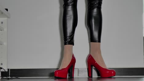 a woman in shiny black leggings walks into the picture and shows her red shimmering high-heeled stilettos