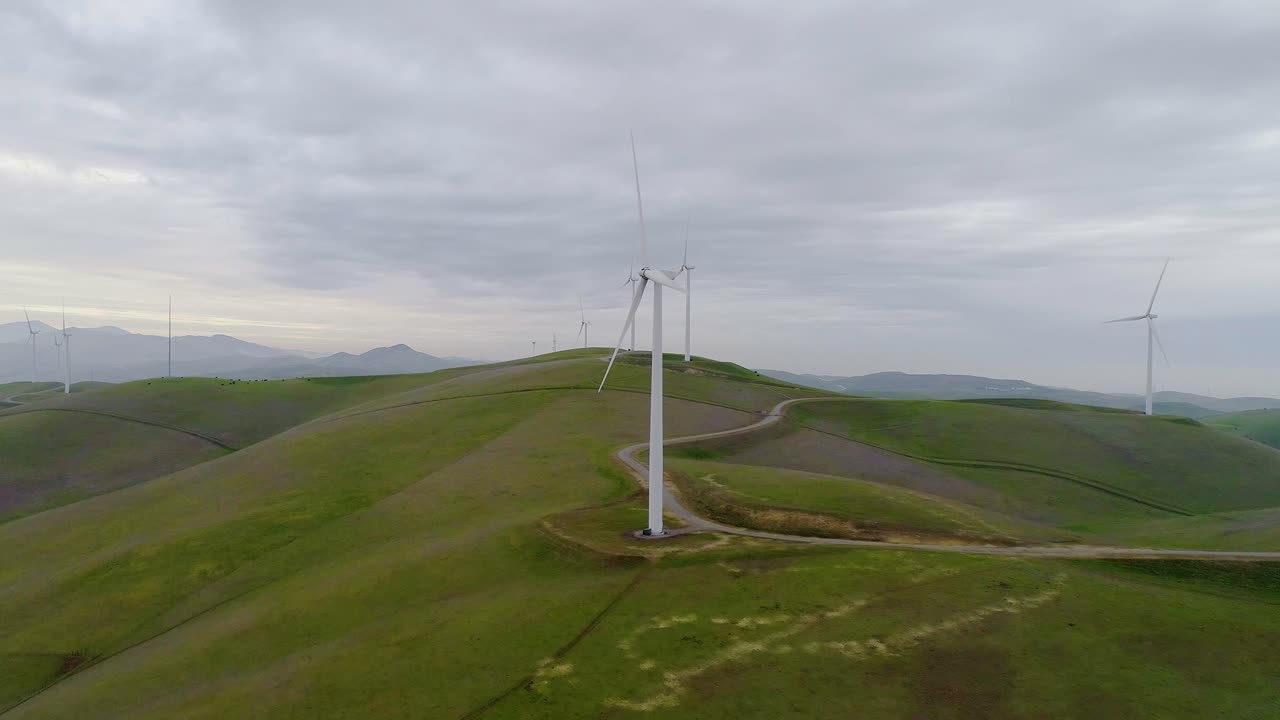 Forward Dolly Closely approaching Wind Turbines atop a Hill with Distant Smokey Mountain Mist at Dusk