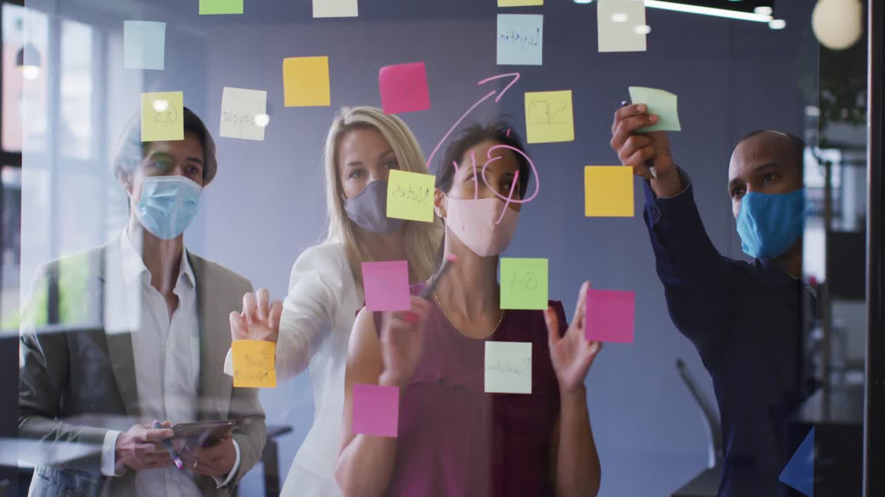 Diverse business colleagues wearing face masks standing brainstorming in office