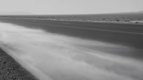dust and sand blowing across a desolate desert road in black and white