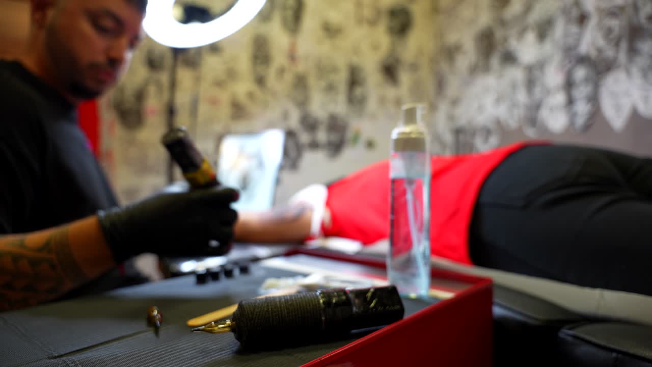 Tattoo artist studio focused while man is tattooing in background