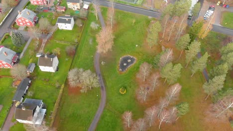 drone footage flying over a small parque with some redo houses on the left hand side ending up over a football field