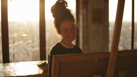 lovely and sophisticated female artist in her 20's is smiling and laughing while drawing picture on easel