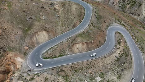 aerial drone shot of a narrow, winding mountain road with multiple cars making their way through.