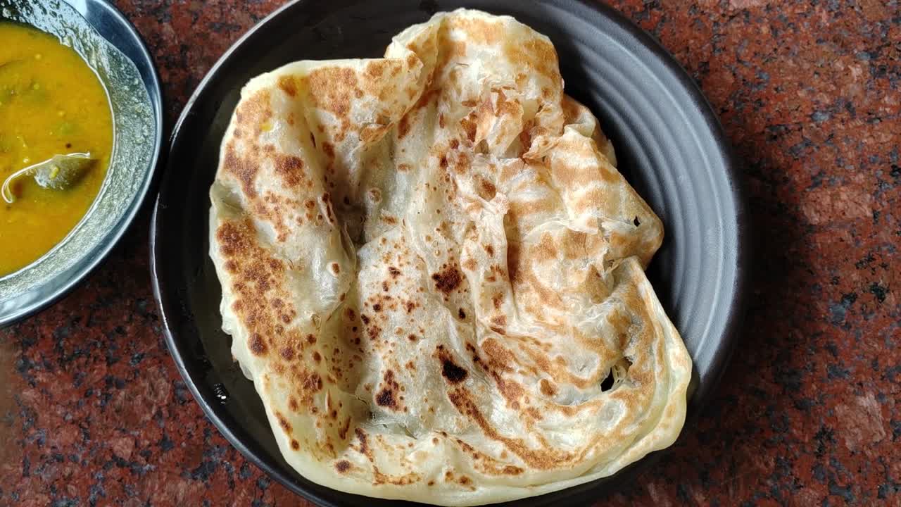 A serving of roti canai, a popular Malaysian dish, placed on a table with a side of dhal curry. A simple and beloved breakfast choice.